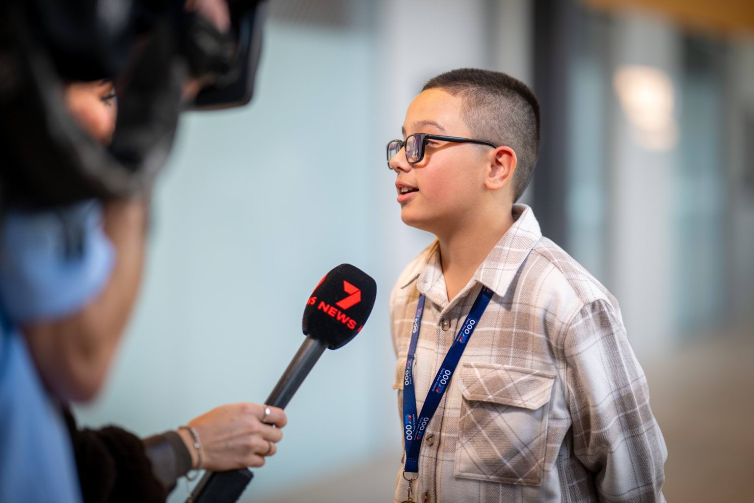 A young boy with glasses being interviewed by a news reporter