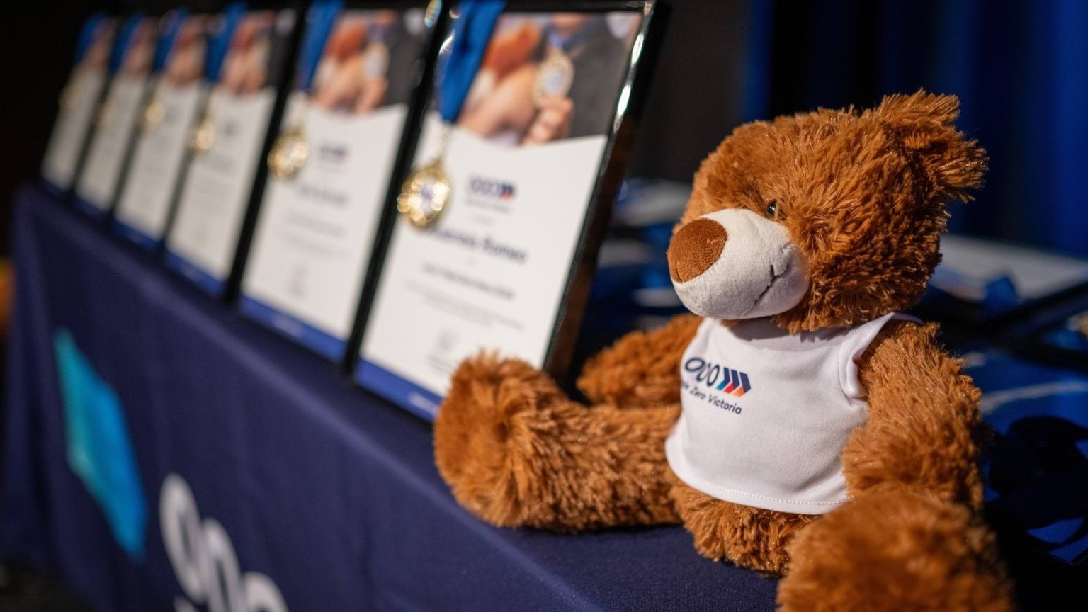 Benny the Bear the Junior Triple Zero Heroes Mascot sitting alongside the certificate and medal