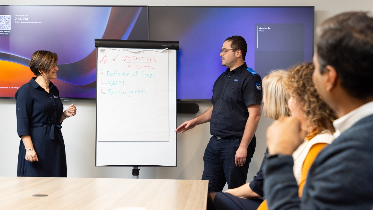 A female and male standing in front of a group of people giving a presentation