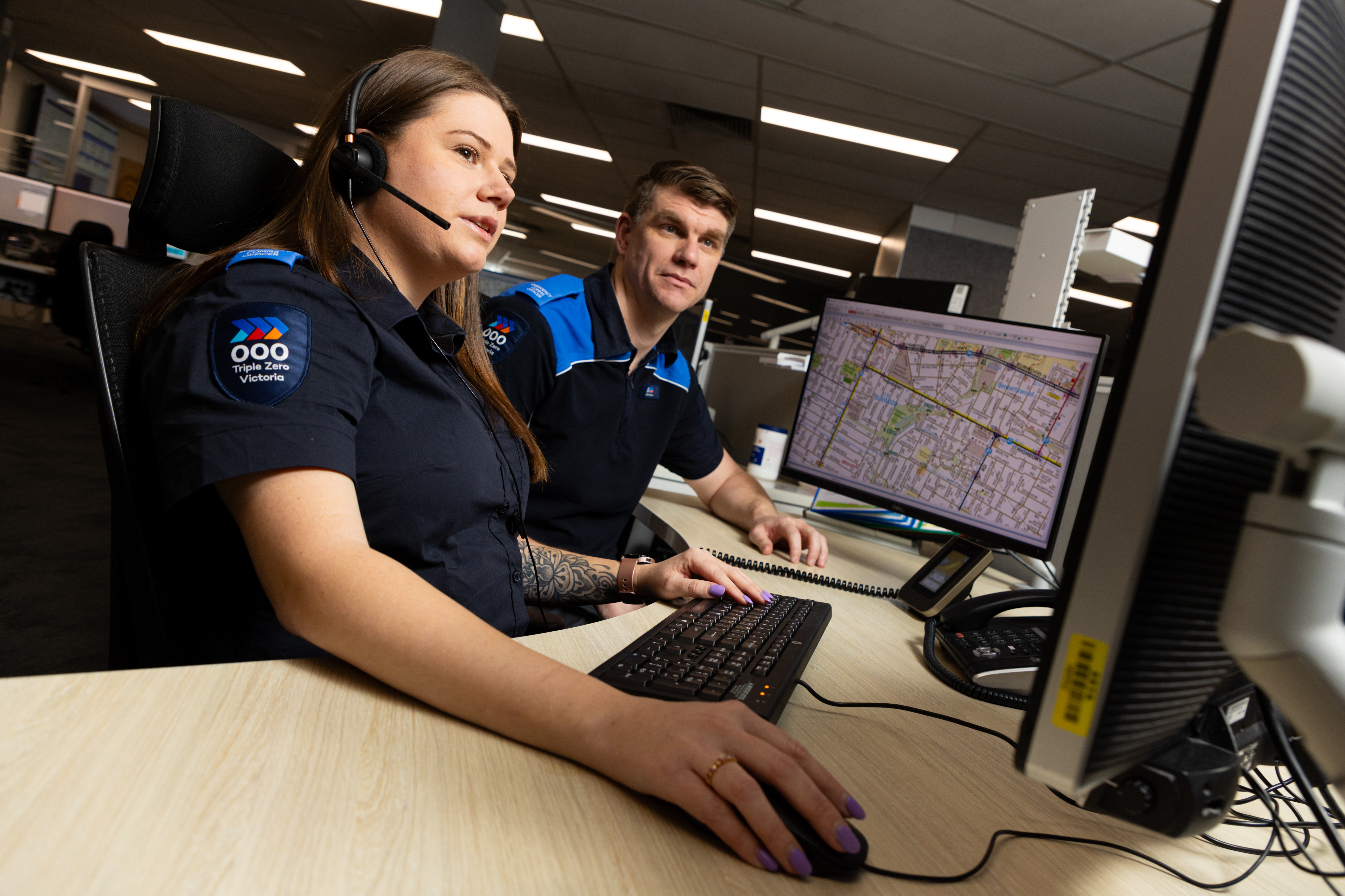 A female Call-Taker sitting at her desk with a male leader sitting next to her providing guidance. 